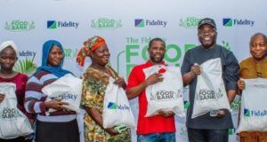 Eti-Osa Community Joins Others To Enjoy Fidelity Bank’s Food Bank Largesse …Henry Asiegbu, Divisional Head, Operations, Fidelity Bank Plc (Left); Adebayo Adeyinka, Executive Technical Assistant to the Managing Director/Chief Executive Officer, Fidelity Bank Plc (5th from Left); Meksley Nwagboh, Divisional Head, Brand and Communications, Fidelity Bank Plc (Right); flanked by some of the beneficiaries at the Fidelity Food Bank outreach in Eti Osa Local Government Area, Lagos recently…