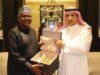 Saudi Envoy, Dangote Meet To Deepen Cooperation, Partnership Two men in traditional robes present an open box with gold-colored items inside, in a formal room.