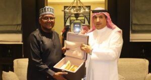 Saudi Envoy, Dangote Meet To Deepen Cooperation, Partnership Two men in traditional robes present an open box with gold-colored items inside, in a formal room.