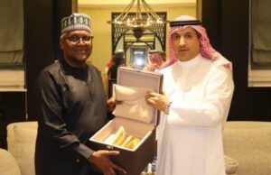 Saudi Envoy, Dangote Meet To Deepen Cooperation, Partnership Two men in traditional robes present an open box with gold-colored items inside, in a formal room.