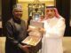Saudi Envoy, Dangote Meet To Deepen Cooperation, Partnership Two men in traditional robes present an open box with gold-colored items inside, in a formal room.