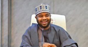 FG Never Introduced Fresh Tax On Vehicles– NRS Smiling man in traditional gray attire and patterned cap sits at a conference table with a microphone in front of him.