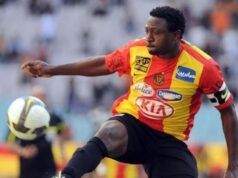 Ex-Super Eagles Striker Slumps, Dies During Training In Kaduna Soccer player in a red and yellow jersey kicking a ball during a match, with blurred stadium stands in the background.