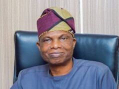 Oyo Govt. Launches Free Evening Market Classes To Tackle Out-Of-School Menace Man wearing a purple‑green headwrap and blue traditional outfit, seated in a dark leather chair.