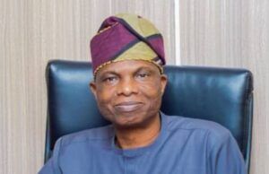 Oyo Govt. Launches Free Evening Market Classes To Tackle Out-Of-School Menace Man wearing a purple‑green headwrap and blue traditional outfit, seated in a dark leather chair.