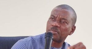 FCAIB Holds Formal Inauguration, Induction Of ACTU Man in a blue striped shirt speaks into a handheld microphone at a panel or meeting table with papers nearby.