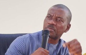 FCAIB Holds Formal Inauguration and Induction Of ACTU Man in a blue striped shirt speaks into a handheld microphone at a panel or meeting table with papers nearby.