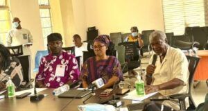LASSA FEVER: Oyo Govt Confirms 5 Cases, Records 1 Death Diverse group of adults seated around a conference table in a bright room; a man speaks into a microphone while others listen, with notebooks, water bottles, and hand sanitizer on the table.