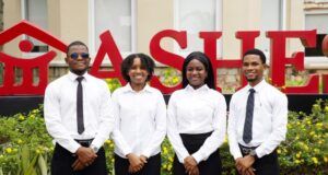 At A4S 2026, Dangote Cement Powers Global Sustainability Innovation Four professionally dressed staff (two men, two women) stand in front of a red 'SALE' sign outside a store.