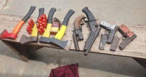 Oyo Police Foil Cult Attack At Ibadan Poly Assorted hand tools laid out on a wooden workbench, including axes, hammers, pliers, and wrenches, with a red cloth on the ground nearby.