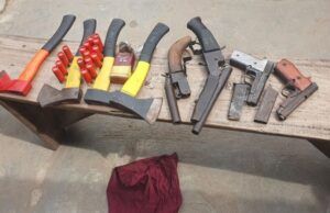 Oyo Police Foil Cult Attack At Ibadan Poly Assorted hand tools laid out on a wooden workbench, including axes, hammers, pliers, and wrenches, with a red cloth on the ground nearby.