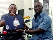 2027: Adekanmbi Visits Ayefele, Pledges To Consolidate On Makinde’s Achievements Two men share a moment in a bright office: one in a wheelchair smiles while handing a blue gift box to a man in a blue shirt who sits nearby. The box has a circular sticker on its front.
