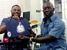 2027: Adekanmbi Visits Ayefele, Pledges To Consolidate On Makinde’s Achievements Two men share a moment in a bright office: one in a wheelchair smiles while handing a blue gift box to a man in a blue shirt who sits nearby. The box has a circular sticker on its front.