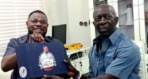 2027: Adekanmbi Visits Ayefele, Pledges To Consolidate On Makinde’s Achievements Two men share a moment in a bright office: one in a wheelchair smiles while handing a blue gift box to a man in a blue shirt who sits nearby. The box has a circular sticker on its front.