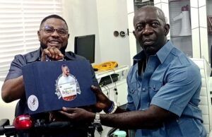 2027: Adekanmbi Visits Ayefele, Pledges To Consolidate On Makinde’s Achievements Two men share a moment in a bright office: one in a wheelchair smiles while handing a blue gift box to a man in a blue shirt who sits nearby. The box has a circular sticker on its front.