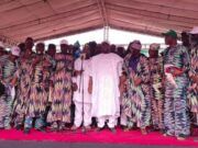 Adelabu Declares Gubernatorial Ambition As Oyo APC Leaders Endorse Him for 2027 Group of people on a stage at a ceremony, many in colorful patterned outfits, with a man in white at center by a microphone.