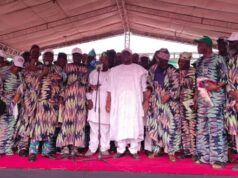 Adelabu Declares Gubernatorial Ambition As Oyo APC Leaders Endorse Him for 2027 Group of people on a stage at a ceremony, many in colorful patterned outfits, with a man in white at center by a microphone.