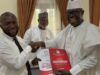 Arapaja Officially Joins Oyo Governorship Race, Submits Nomination Forms Three men in white traditional outfits shake hands during a presentation, the man on the right holding a red government report titled Governance while another man smiles in the background.