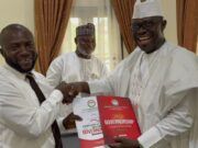Arapaja Officially Joins Oyo Governorship Race, Submits Nomination Forms Three men in white traditional outfits shake hands during a presentation, the man on the right holding a red government report titled Governance while another man smiles in the background.
