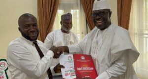 Arapaja Officially Joins Oyo Governorship Race, Submits Nomination Forms Three men in white traditional outfits shake hands during a presentation, the man on the right holding a red government report titled Governance while another man smiles in the background.