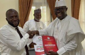 Arapaja Officially Joins Oyo Governorship Race, Submits Nomination Forms Three men in white traditional outfits shake hands during a presentation, the man on the right holding a red government report titled Governance while another man smiles in the background.
