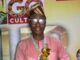 August24news.com Publisher, Ajagbe, Bags Media Personality Award Smiling man in a pink traditional outfit and head wrap holding a gold star trophy on stage.