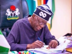 Tinubu’s Govt To Scrap JSS/SSS Structure Over 20m Dropouts Nigerian official signing documents at a desk, with the coat of arms on the chair behind him.