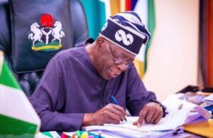 Tinubu’s Govt To Scrap JSS/SSS Structure Over 20m Dropouts Nigerian official signing documents at a desk, with the coat of arms on the chair behind him.