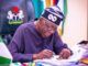Excitement As Tinubu Flags Off Concrete Construction For 82km Osogbo/Iwo/Ibadan, 88km Osogbo/Gbongan Roads Nigerian official signing documents at a desk, with the coat of arms on the chair behind him.