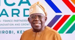 Content Exploitation: Tinubu Hailed By NPO For Directing FCCPC To Investigate Big Tech, AI Platforms Smiling man in tan traditional attire and head wrap posing in front of an Africa-France partnership banner at a formal event