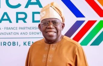 Content Exploitation: Tinubu Hailed By NPO For Directing FCCPC To Investigate Big Tech, AI Platforms Smiling man in tan traditional attire and head wrap posing in front of an Africa-France partnership banner at a formal event