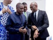 No Rift With Tony Elumelu, Dangote Group Claims Four men in formal clothing chat and smile at an indoor event; two are foreground, one in a navy traditional outfit and one in a black suit.