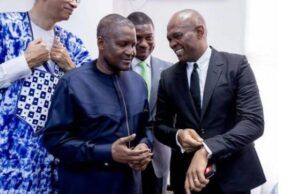 No Rift With Tony Elumelu, Dangote Group Claims Four men in formal clothing chat and smile at an indoor event; two are foreground, one in a navy traditional outfit and one in a black suit.