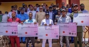 Ekiti Govt Disburses N29m Subvention To Youth, Student Groups Group of men and women proudly holding oversized ceremonial cheques during a development grant event outdoors.