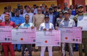 Ekiti Govt Disburses N29m Subvention To Youth, Student Groups Group of men and women proudly holding oversized ceremonial cheques during a development grant event outdoors.