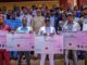 Ekiti Govt Disburses N29m Subvention To Youth, Student Groups Group of men and women proudly holding oversized ceremonial cheques during a development grant event outdoors.
