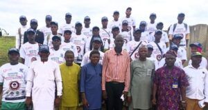 TECH-U VC Commends Hon. Oluwafowokanmi At Flag-Off Of Technical Trainers Recruitments, Training Programme Group of graduates in white T-shirts and caps posing on steps outdoors, with a few officials in colorful outfits standing at the front.