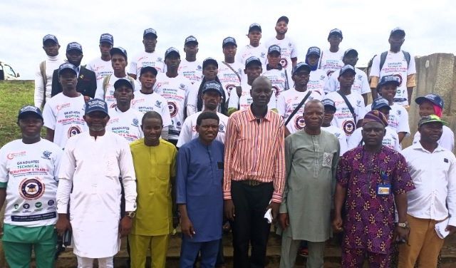 Fowokanmi enpowerment Group of graduates in white T-shirts and caps posing on steps outdoors, with a few officials in colorful outfits standing at the front.
