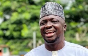 APC Primaries: Abdulganeey Adekunle, ‘Mr. GRA,’Secures House Of Assembly Ticket Smiling man wearing a white traditional outfit with gold trim and a patterned cap outdoors in greenery.