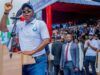 Gov. Makinde Is Capable Of Leading Nigeria — Oyo ALGON Chairman Man at a podium raising his finger while speaking at an outdoor rally, with a crowd and officials behind him.