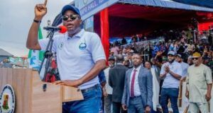 Gov. Makinde Is Capable Of Leading Nigeria — Oyo ALGON Chairman Man at a podium raising his finger while speaking at an outdoor rally, with a crowd and officials behind him.