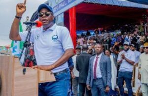Gov. Makinde Is Capable Of Leading Nigeria — Oyo ALGON Chairman Man at a podium raising his finger while speaking at an outdoor rally, with a crowd and officials behind him.