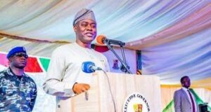 Makinde Declares Presidential Ambition Ahead Of 2027 Elections Governor in traditional attire speaking at a podium with the Oyo State seal, flanked by security personnel at an outdoor event.