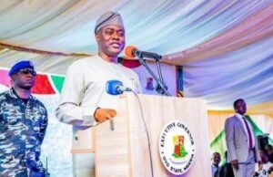 Makinde Declares Presidential Ambition Ahead Of 2027 Elections Governor in traditional attire speaking at a podium with the Oyo State seal, flanked by security personnel at an outdoor event.