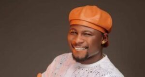 ₦6.56bn Earnings: Kamo State Secures No. 2 Spot In Nollywood Smiling man wearing an orange traditional hat and white lace outfit, giving a thumbs-up gesture toward the camera.