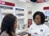 LG Electronics Expands Health Protection For Nigerian Consumers With Free Comprehensive Insurance Two women in an LG store; a sales associate wearing a 'Free Malaria Insurance' shirt shows a tablet to a customer, with LG air-conditioners on the wall behind them.