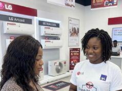LG Electronics Expands Health Protection For Nigerian Consumers With Free Comprehensive Insurance Two women in an LG store; a sales associate wearing a 'Free Malaria Insurance' shirt shows a tablet to a customer, with LG air-conditioners on the wall behind them.