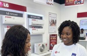 LG Electronics Expands Health Protection For Nigerian Consumers With Free Comprehensive Insurance Two women in an LG store; a sales associate wearing a 'Free Malaria Insurance' shirt shows a tablet to a customer, with LG air-conditioners on the wall behind them.