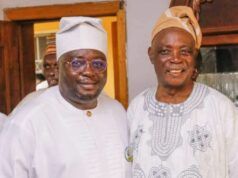 The Stool Is Bigger Than The Ballot: Why Traditional Rulers Must Stay Non-Partisan Two men in traditional West African attire posing and smiling for a photo indoors, one wearing a white agbada and cap with glasses, the other in a patterned tunic and tan cap.