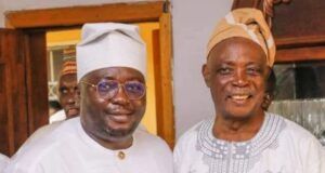 The Stool Is Bigger Than The Ballot: Why Traditional Rulers Must Stay Non-Partisan Two men in traditional West African attire posing and smiling for a photo indoors, one wearing a white agbada and cap with glasses, the other in a patterned tunic and tan cap.